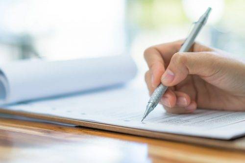 Hand with pen over application form . Hand with pen over application form